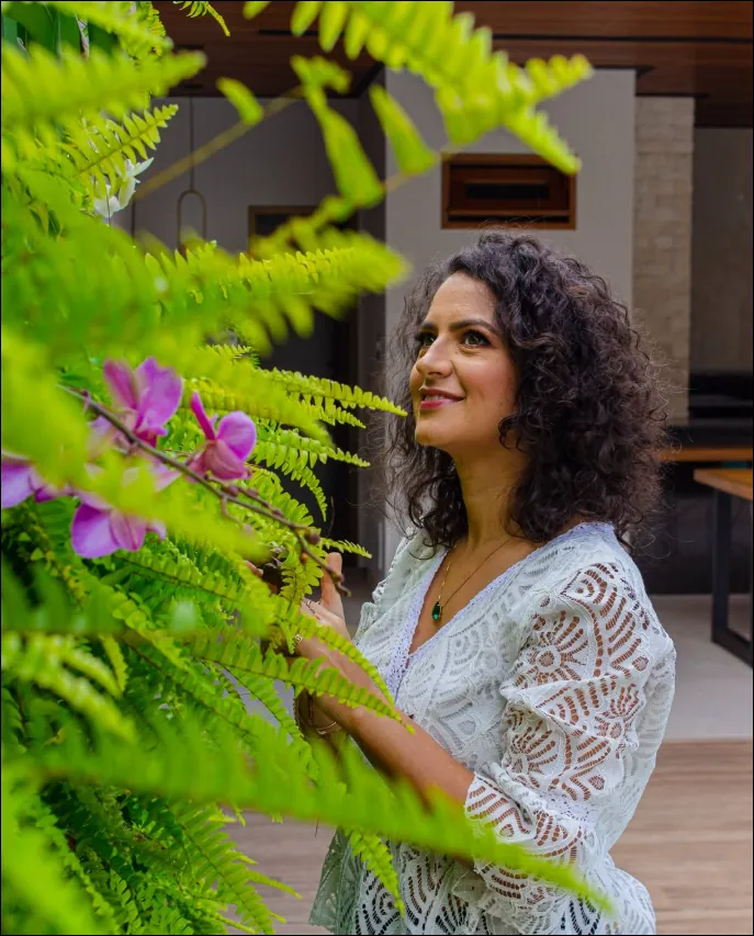 Jordânia Barros entre folhas de costela-de-adão e orquídeas em um jardim