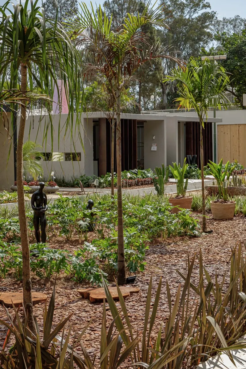 Jardim tropical com palmeiras, esculturas e pavilhão de concreto durante o dia