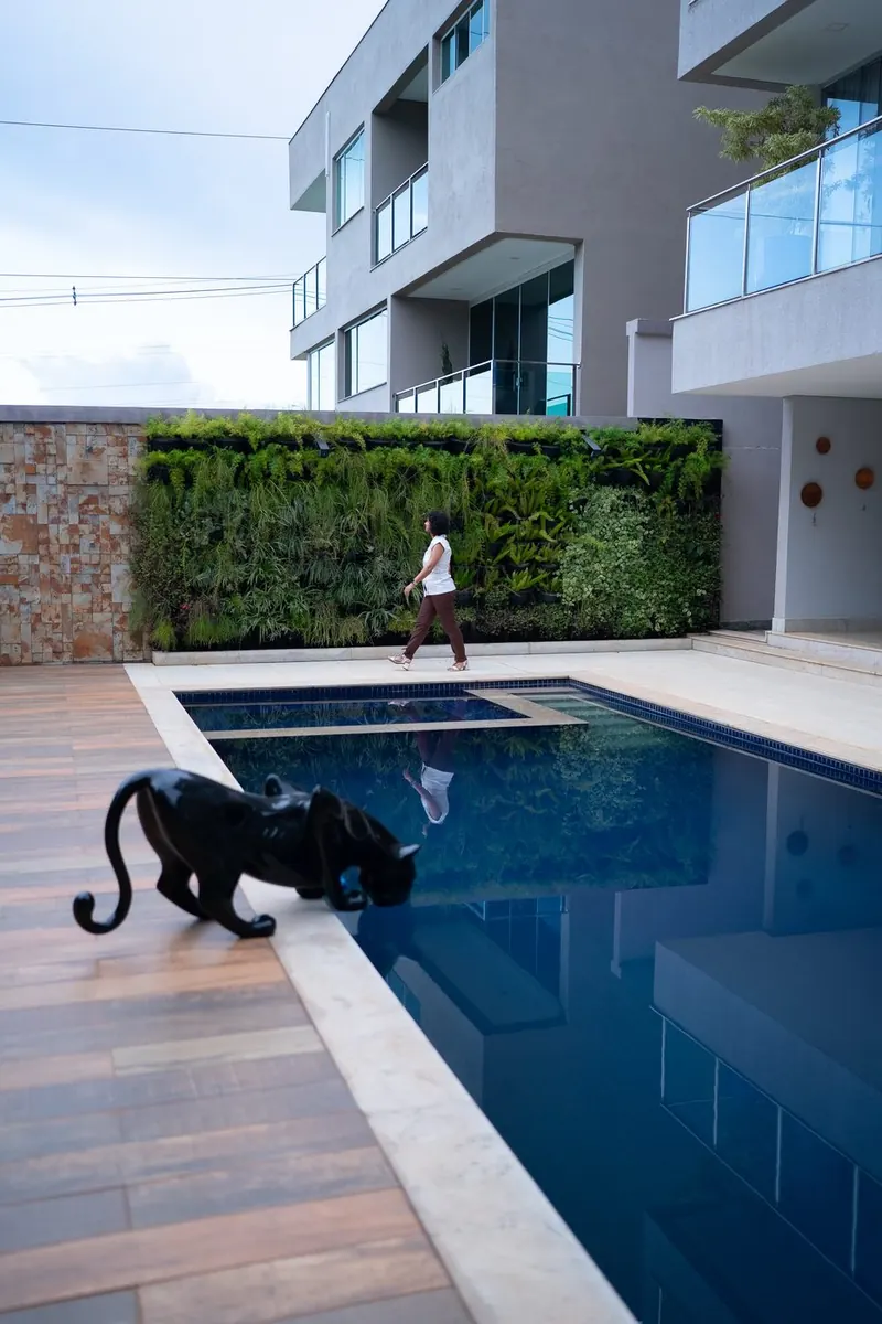 Piscina com deque, escultura de pantera e jardim vertical ao fundo