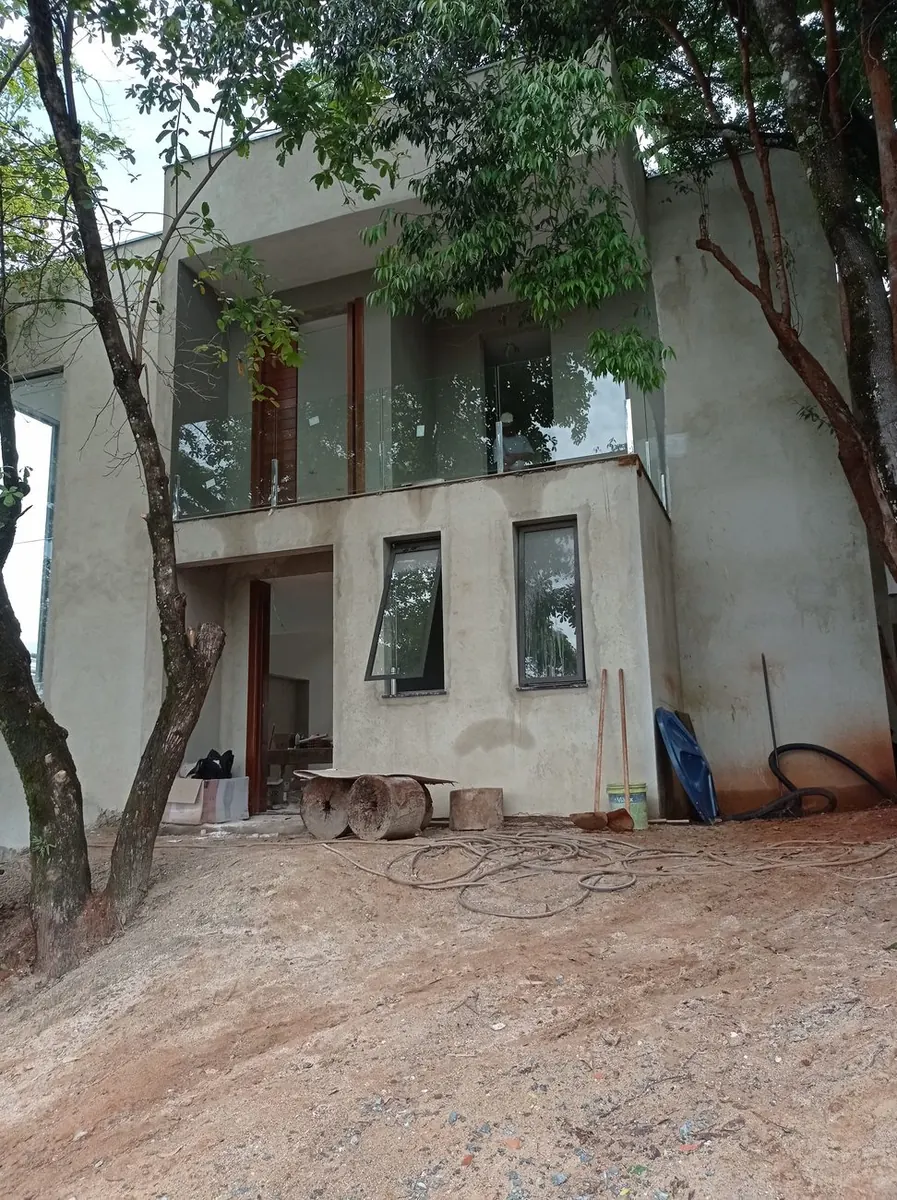 Fachada da casa ainda em obra, com terreno de terra batida e materiais de construção